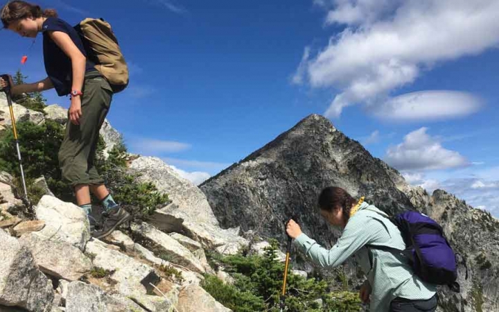 two students ascend over a rocky landscape with a mountain in the background